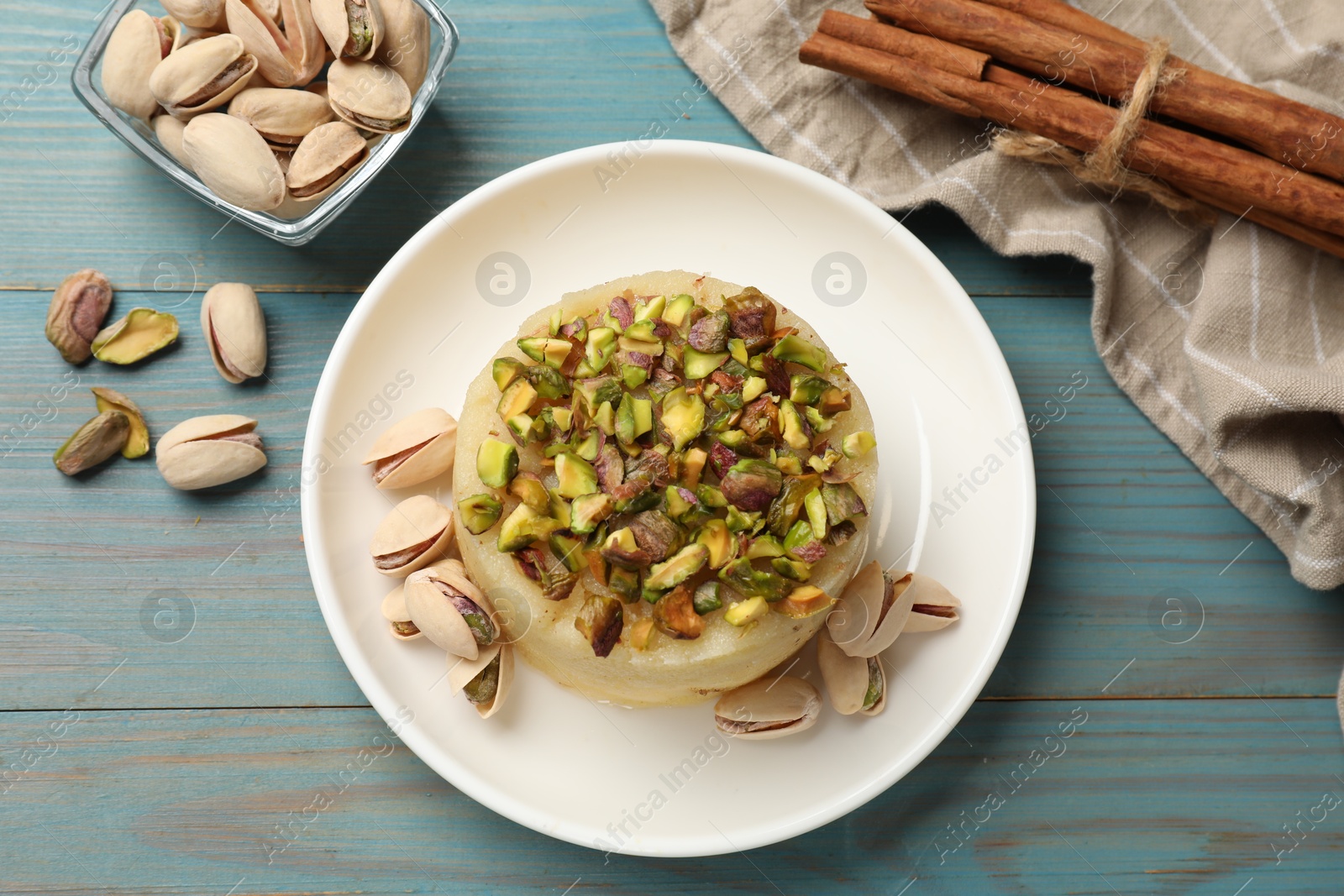 Photo of Delicious sweet semolina halva with pistachios on blue wooden table, flat lay