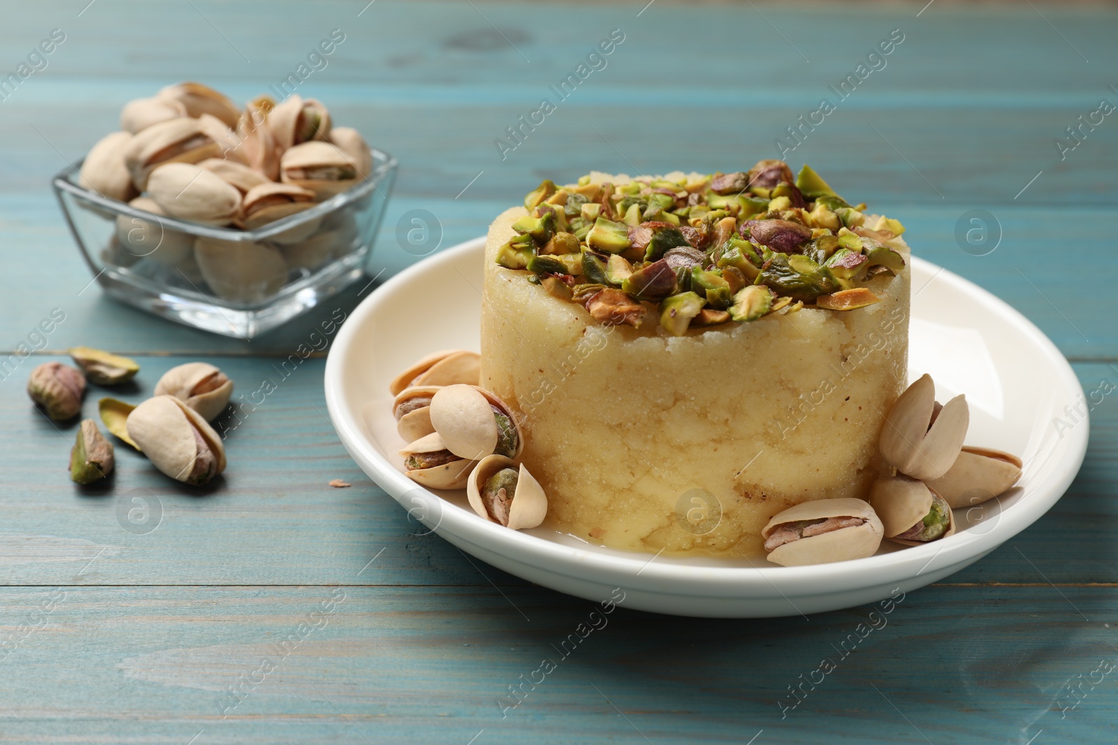 Photo of Delicious sweet semolina halva with pistachios on blue wooden table, closeup