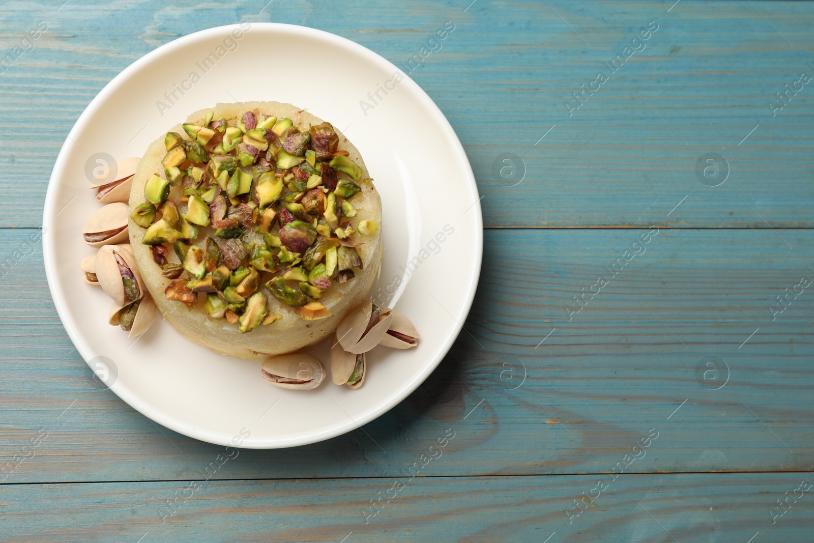 Photo of Delicious sweet semolina halva with pistachios on blue wooden table, top view. Space for text