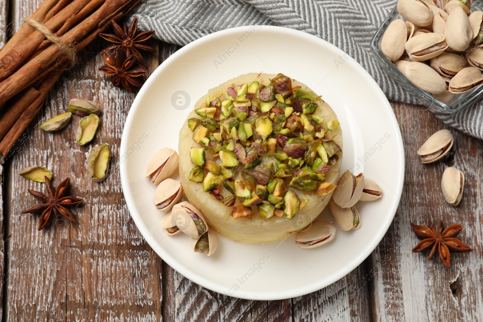 Photo of Delicious sweet semolina halva with pistachios and spices on wooden table, flat lay