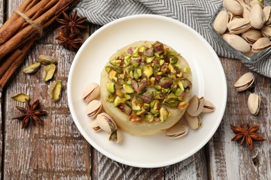 Photo of Delicious sweet semolina halva with pistachios and spices on wooden table, flat lay