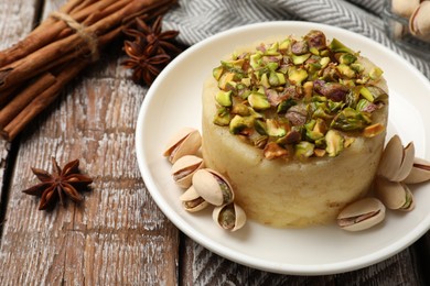 Photo of Delicious sweet semolina halva with pistachios and spices on wooden table, closeup