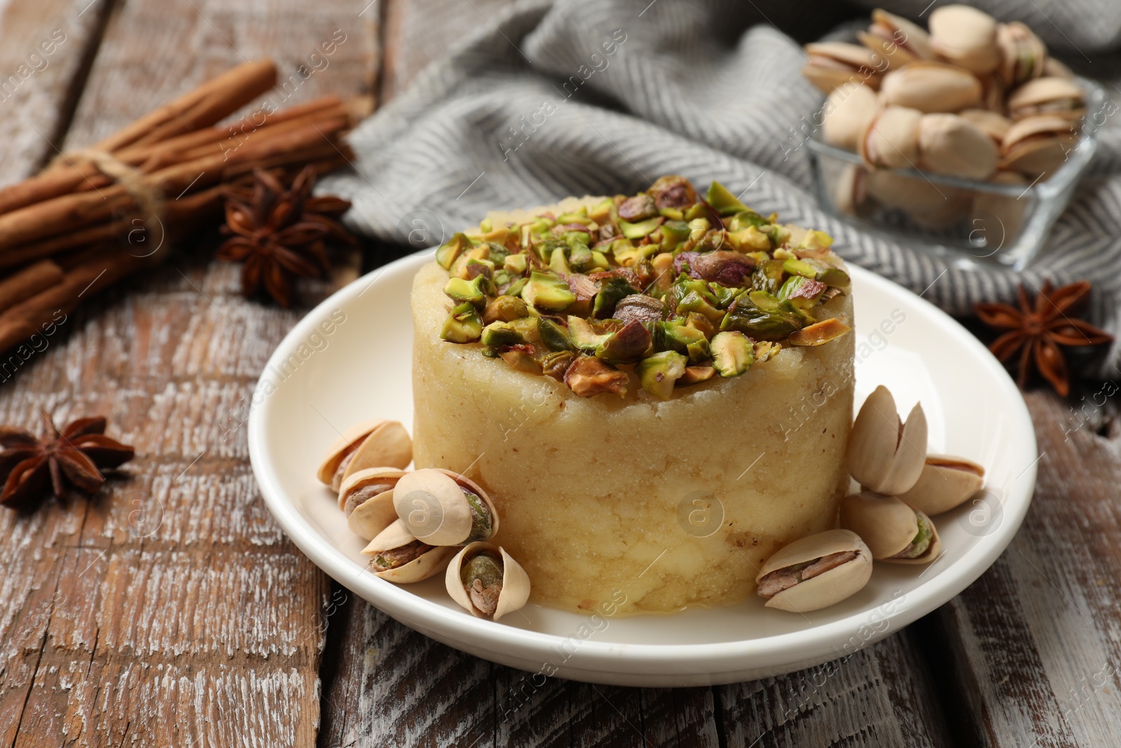 Photo of Delicious sweet semolina halva with pistachios and spices on wooden table, closeup