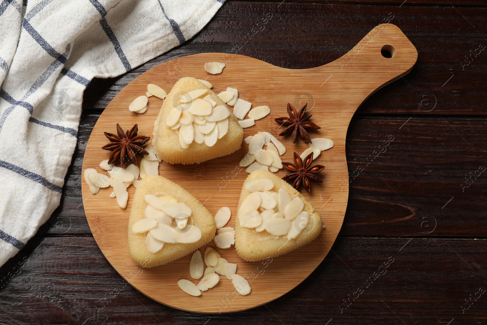 Photo of Pieces of delicious sweet semolina halva with almond flakes and spices on wooden table, top view