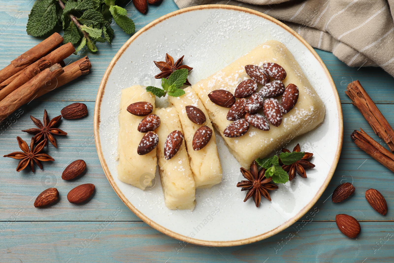 Photo of Delicious sweet semolina halva with almonds, spices and mint on light blue wooden table, flat lay