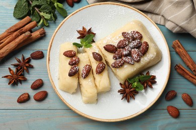 Photo of Delicious sweet semolina halva with almonds, spices and mint on light blue wooden table, flat lay