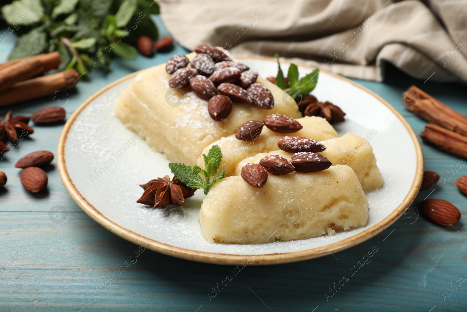 Photo of Delicious sweet semolina halva with almonds, spices and mint on light blue wooden table, closeup