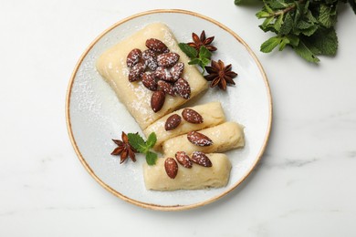 Photo of Delicious sweet semolina halva with almonds, spices and mint on white marble table, top view