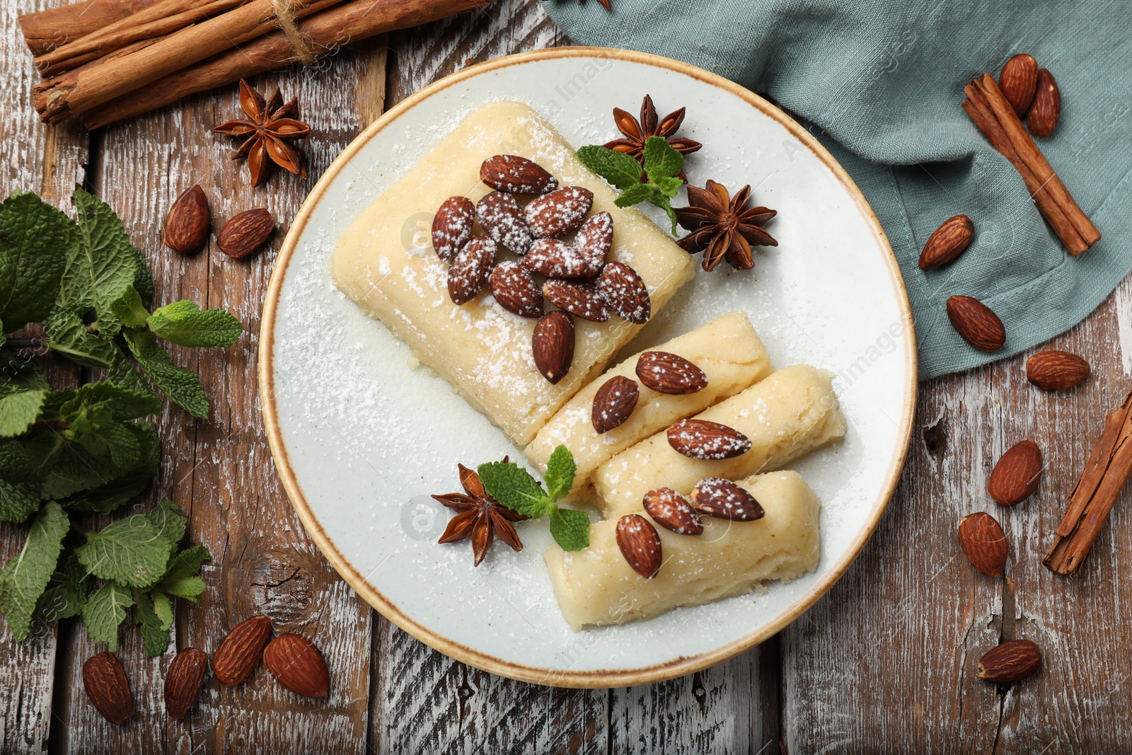 Photo of Delicious sweet semolina halva with almonds, spices and mint on wooden table, flat lay