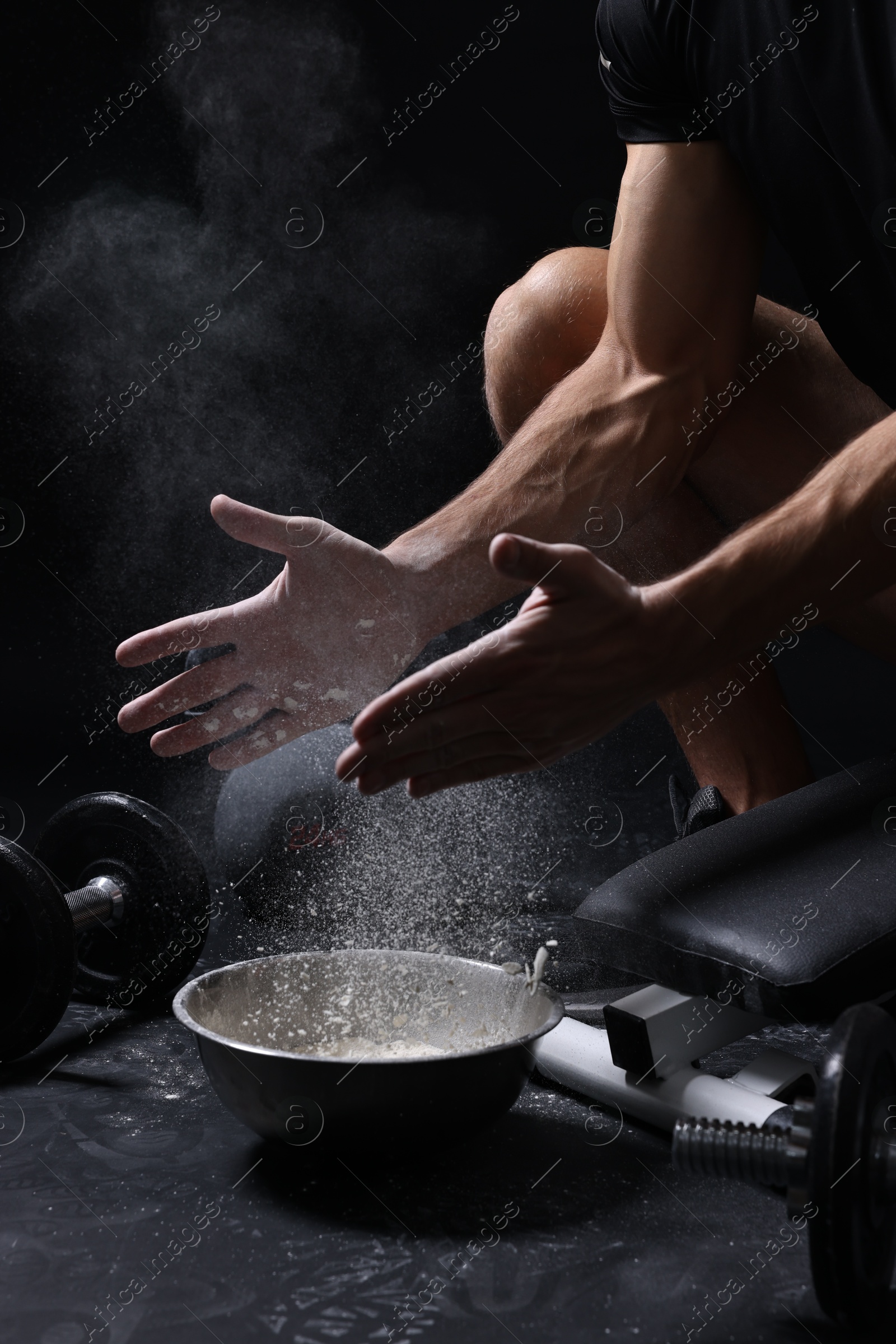 Photo of Man clapping hands with talcum powder above bowl before training on black background, closeup