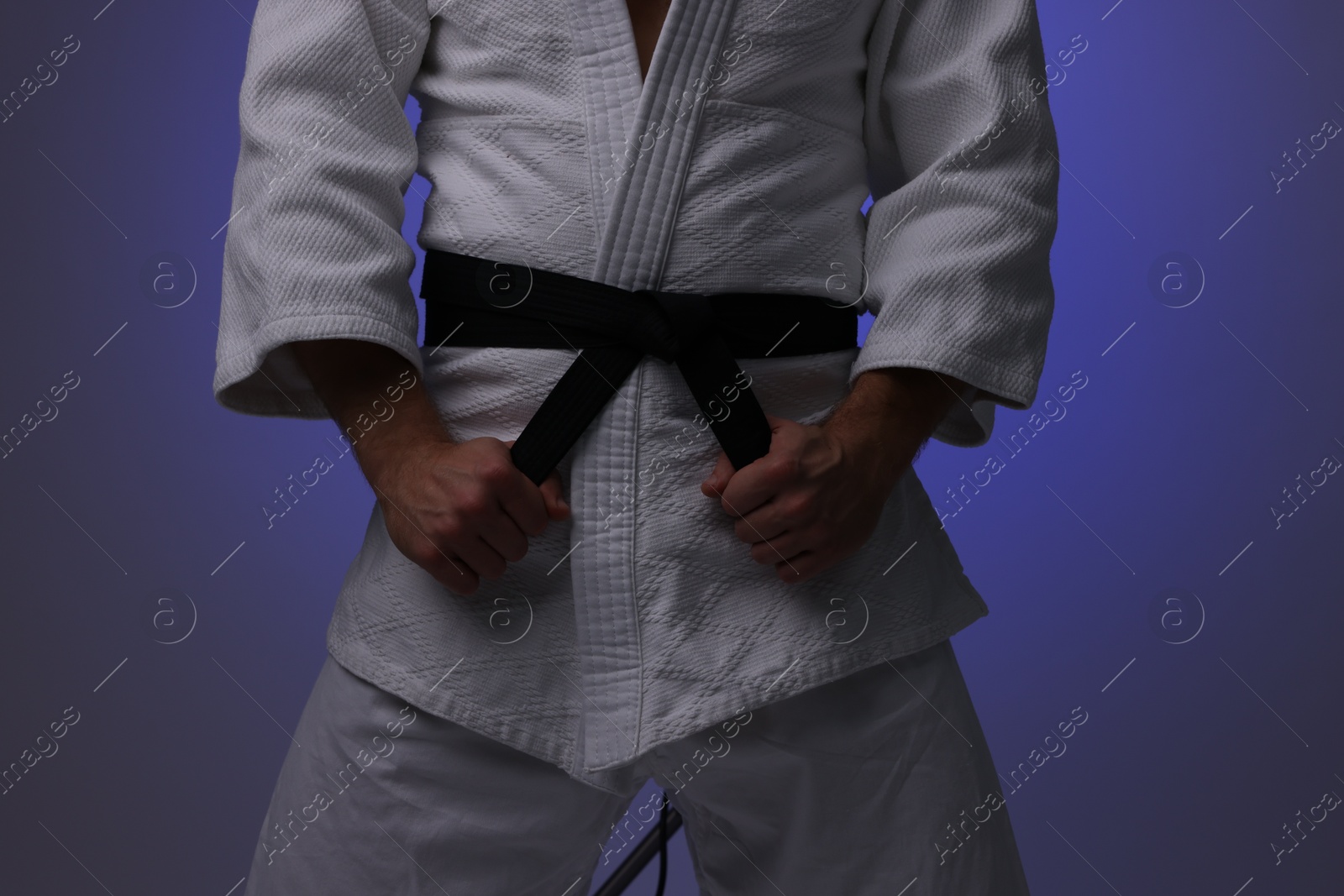 Photo of Karate fighter in uniform on dark purple background, closeup