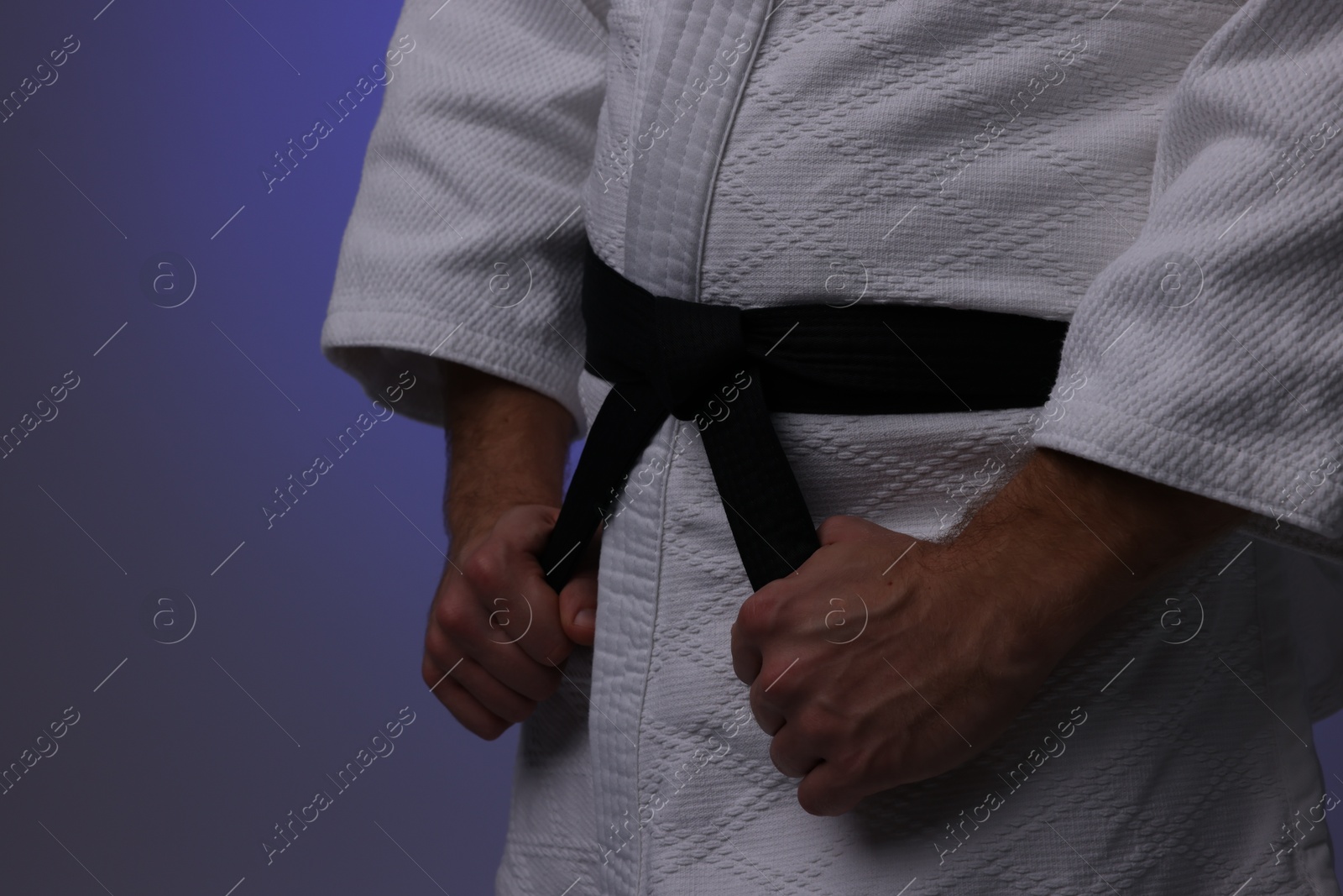 Photo of Karate fighter in uniform on dark purple background, closeup