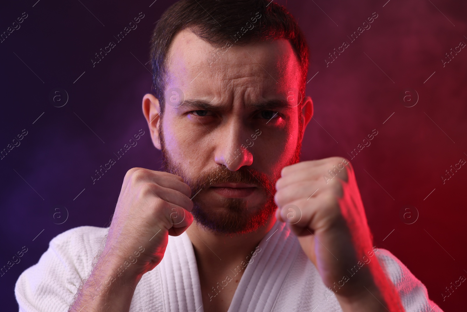 Photo of Karate fighter wearing uniform in color lights and smoke, closeup