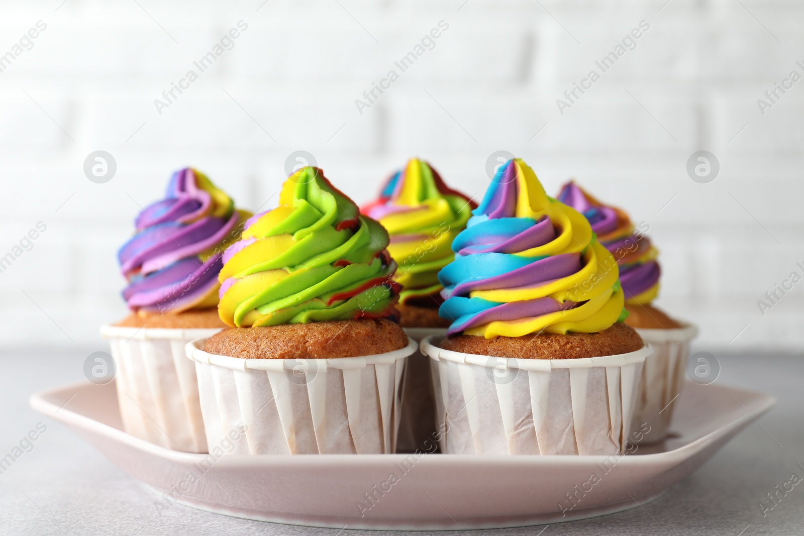 Photo of Tasty cupcakes with colorful cream on light grey table, closeup