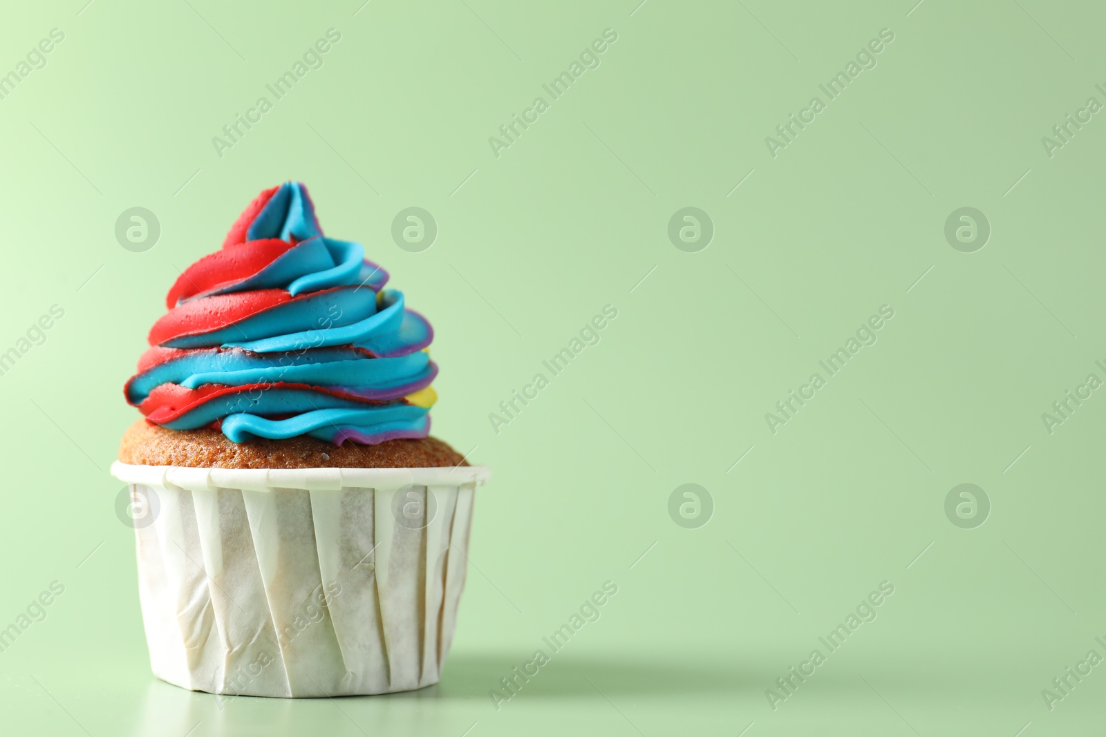 Photo of Tasty cupcake with colorful cream on light green background, closeup. Space for text