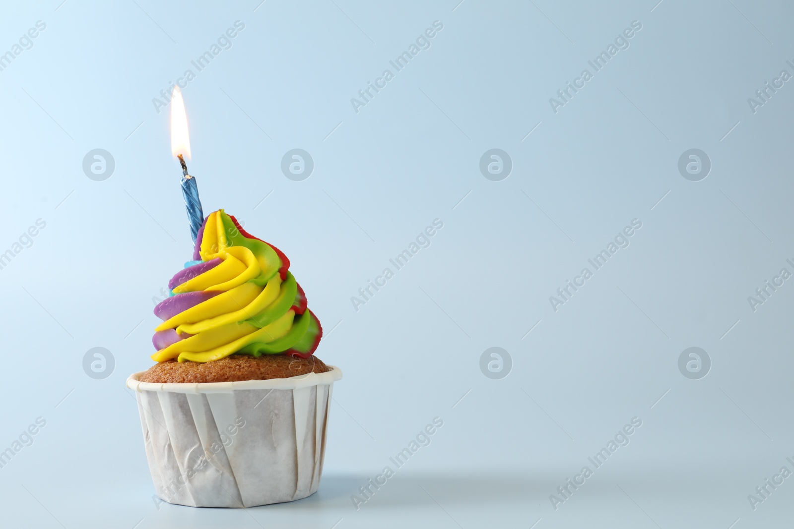 Photo of Tasty cupcake with colorful cream and burning candle on light blue background, space for text