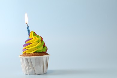 Photo of Tasty cupcake with colorful cream and burning candle on light blue background, space for text