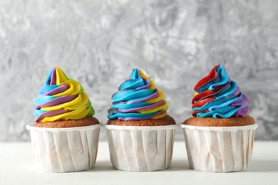 Photo of Delicious cupcakes with colorful cream on white wooden table against blurred grey background, closeup