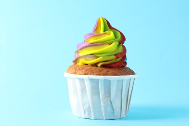 Photo of One delicious cupcake with colorful cream on light blue background, closeup