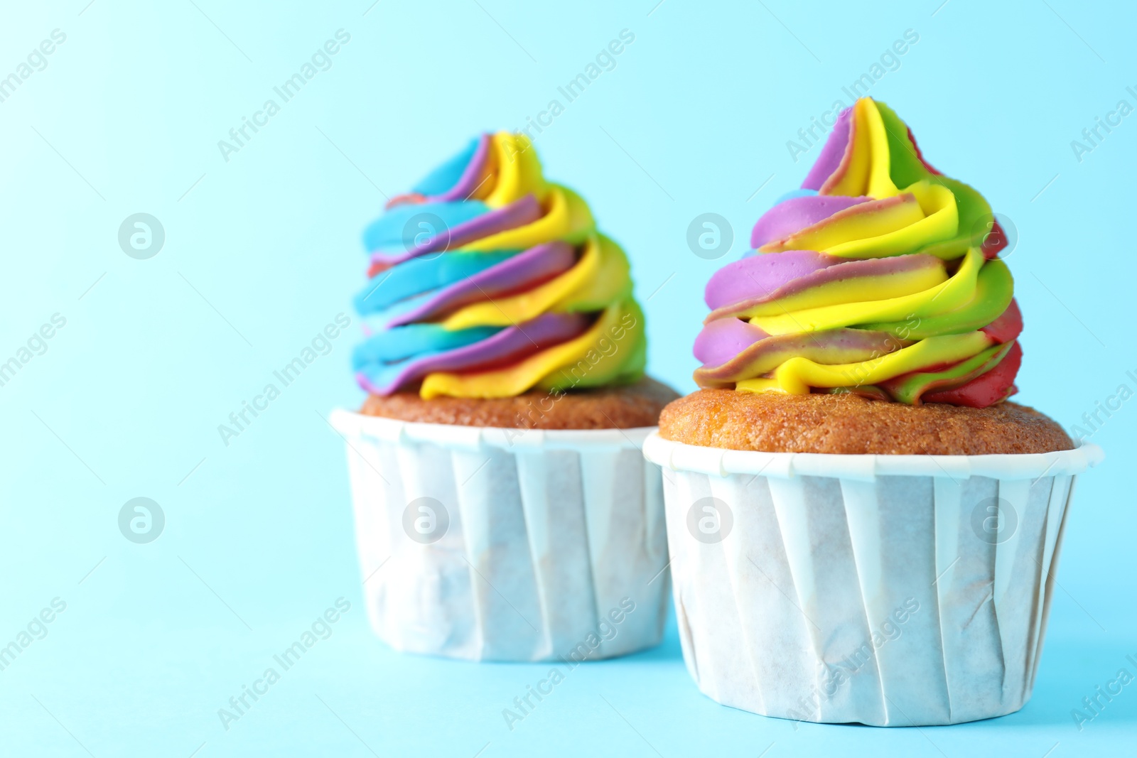 Photo of Delicious cupcakes with colorful cream on light blue background, closeup. Space for text