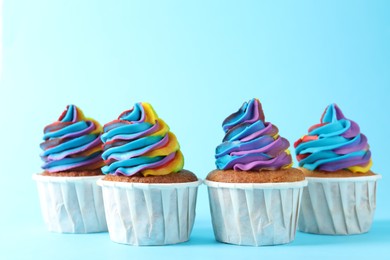 Photo of Delicious cupcakes with colorful cream on light blue background, closeup