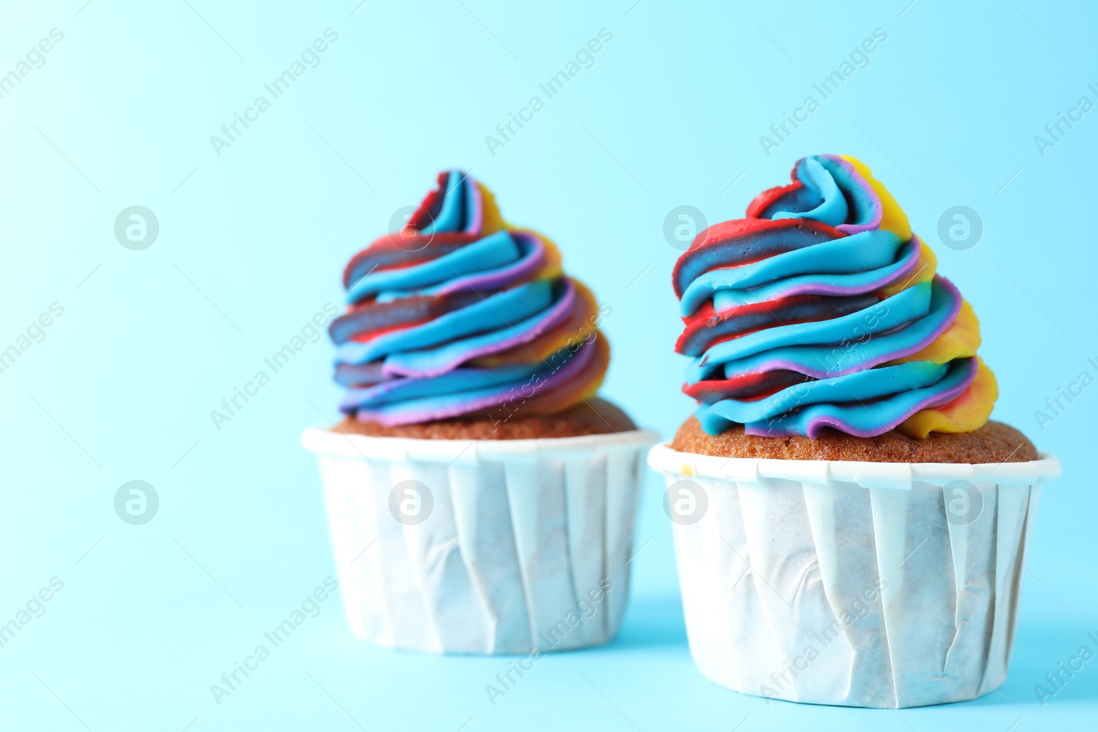 Photo of Delicious cupcakes with colorful cream on light blue background, closeup. Space for text