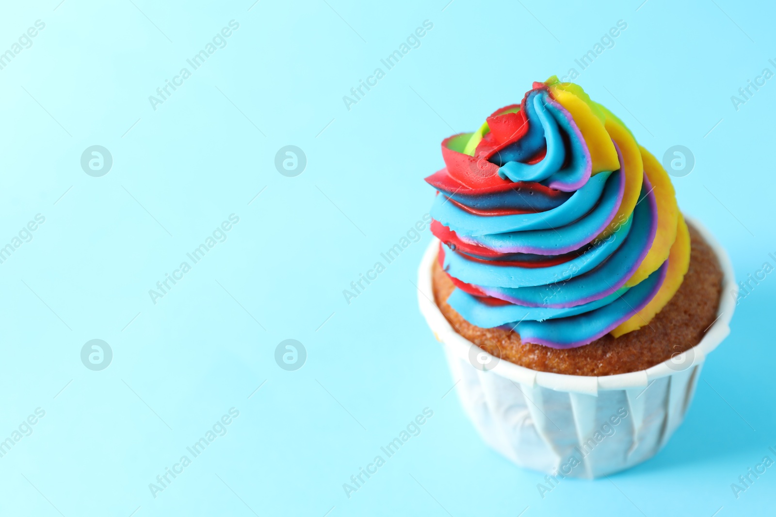 Photo of One delicious cupcake with colorful cream on light blue background, closeup. Space for text