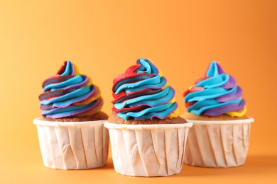 Photo of Delicious cupcakes with colorful cream on orange background, closeup