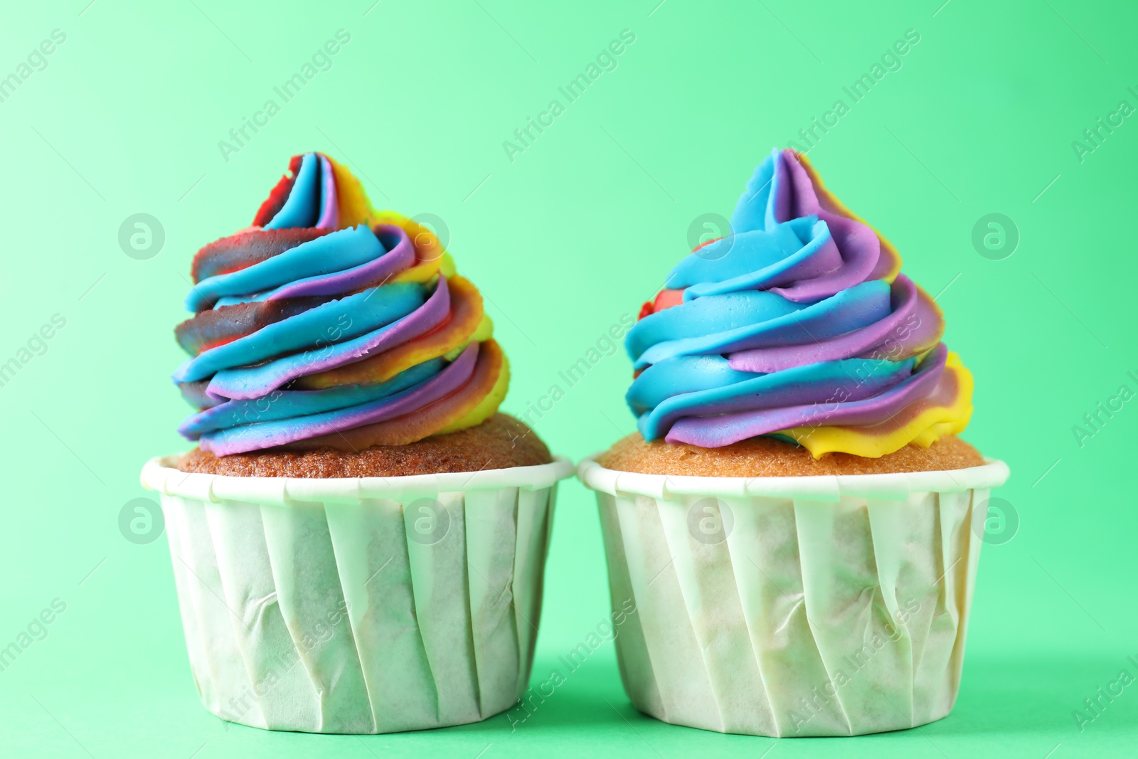 Photo of Delicious cupcakes with colorful cream on green background, closeup