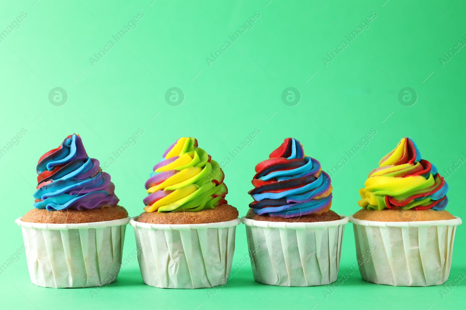 Photo of Delicious cupcakes with colorful cream on green background, closeup