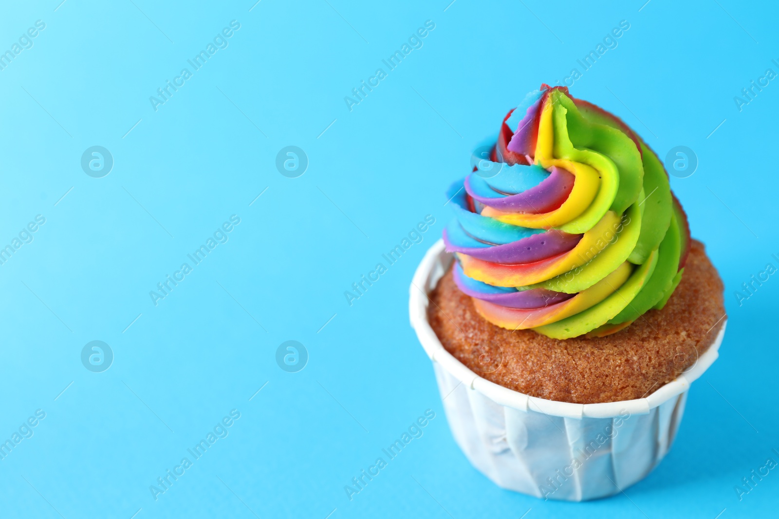 Photo of One delicious cupcake with colorful cream on light blue background, closeup. Space for text