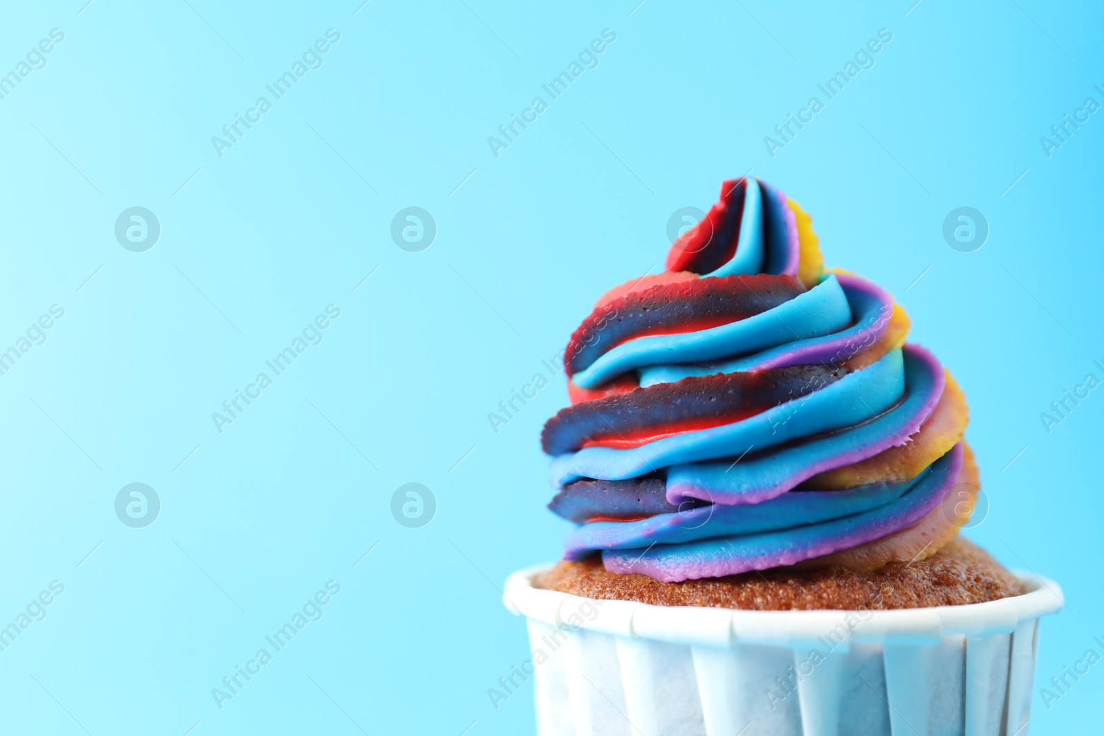 Photo of One delicious cupcake with colorful cream on light blue background, closeup. Space for text