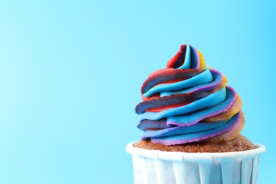 Photo of One delicious cupcake with colorful cream on light blue background, closeup. Space for text