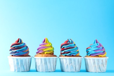 Photo of Delicious cupcakes with colorful cream on light blue background, closeup