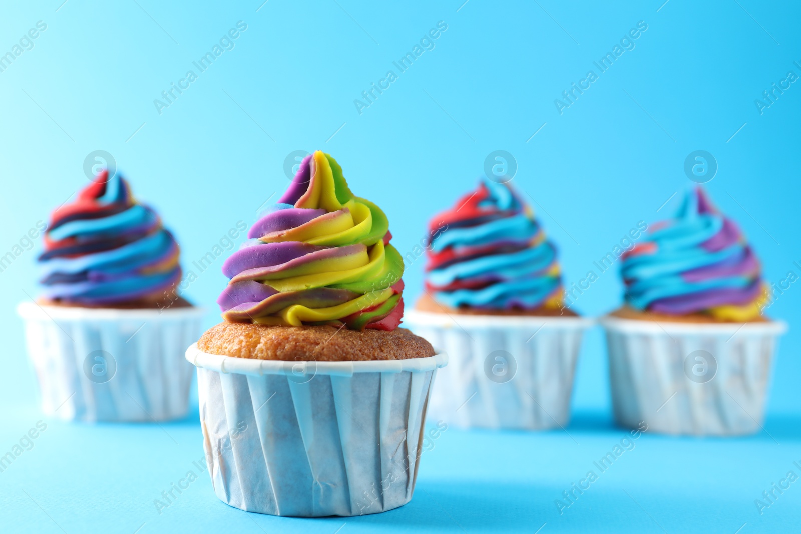 Photo of Delicious cupcakes with colorful cream on light blue background, selective focus