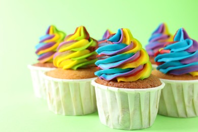 Photo of Delicious cupcakes with colorful cream on light green background, closeup