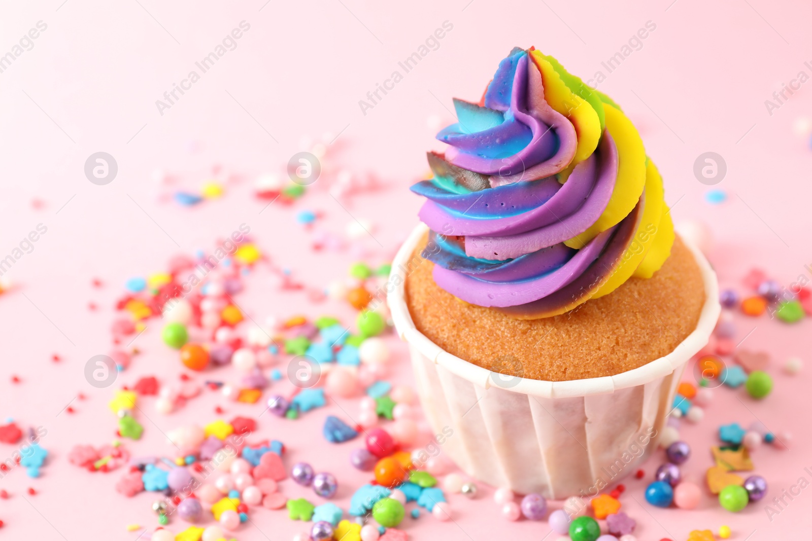 Photo of One delicious cupcake with colorful cream and sprinkles on pink background, closeup. Space for text