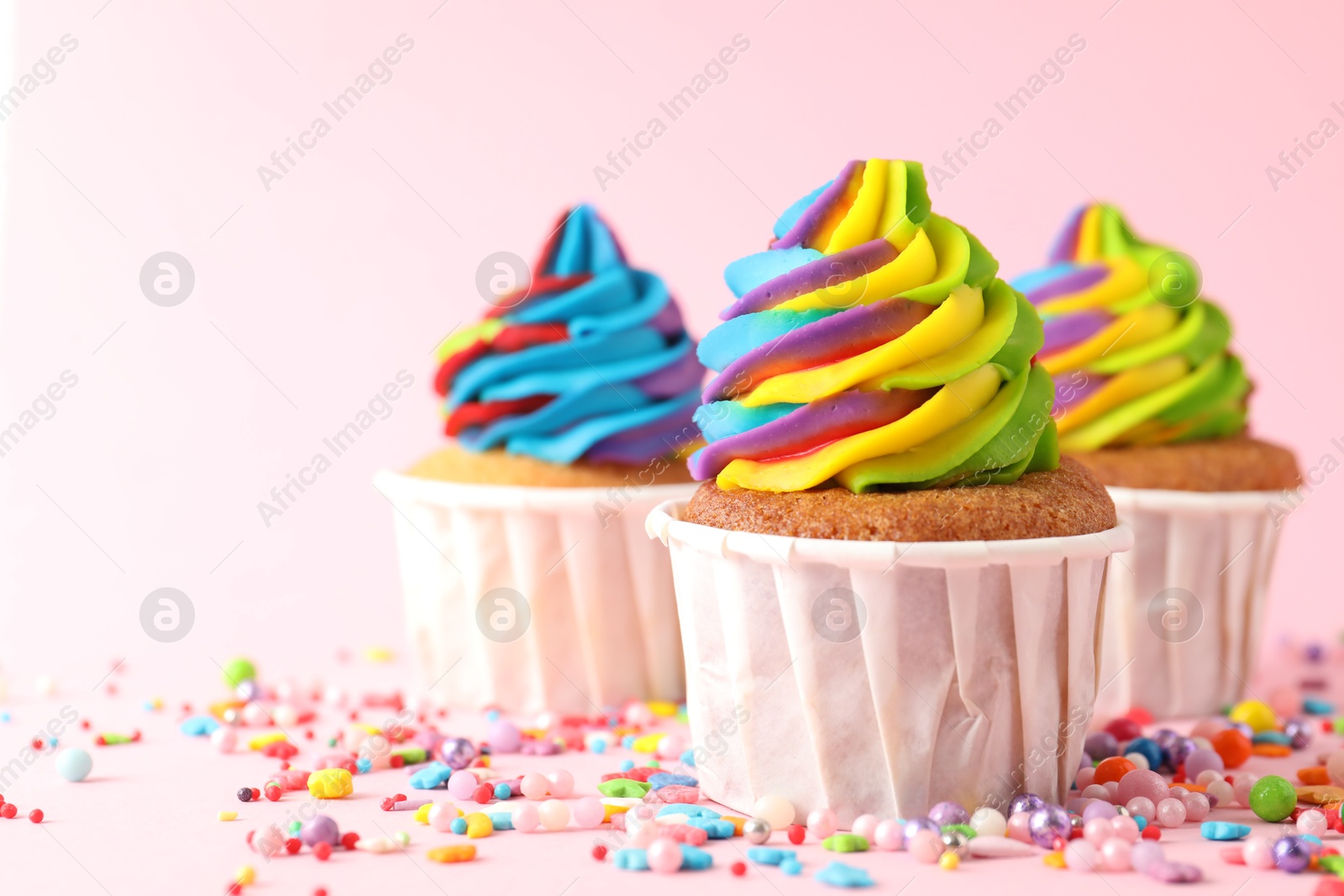 Photo of Delicious cupcakes with colorful cream and sprinkles on pink background, closeup. Space for text