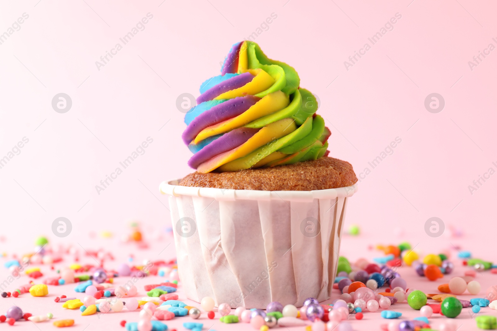 Photo of One delicious cupcake with colorful cream and sprinkles on pink background, closeup