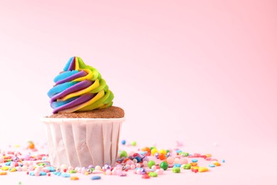 Photo of One delicious cupcake with colorful cream and sprinkles on pink background, closeup. Space for text