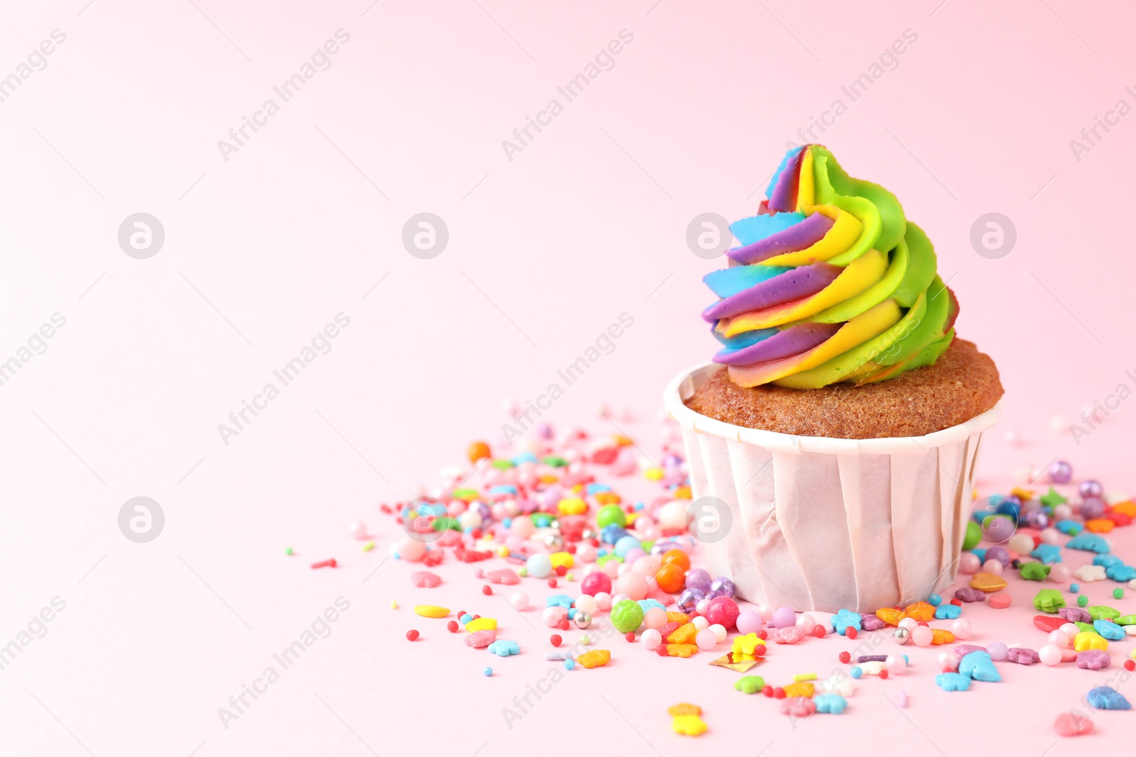 Photo of One delicious cupcake with colorful cream and sprinkles on pink background, closeup. Space for text