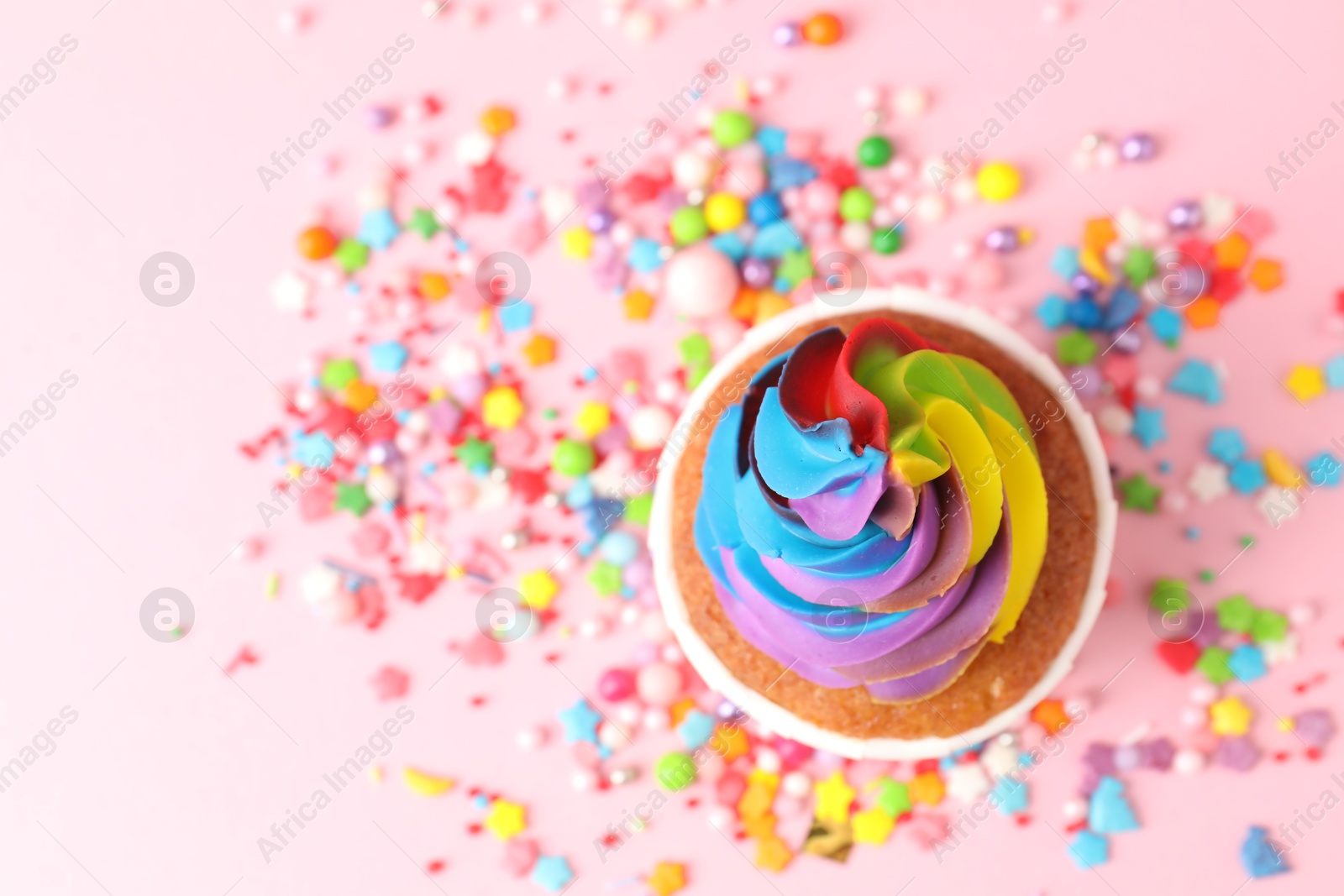 Photo of Delicious cupcake with colorful cream and sprinkles on pink background, top view. Space for text