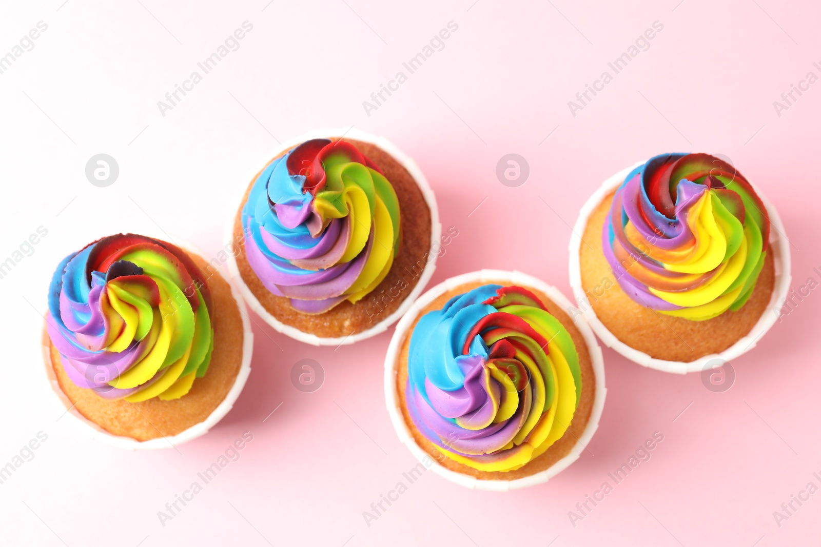 Photo of Delicious cupcakes with colorful cream on pink background, flat lay