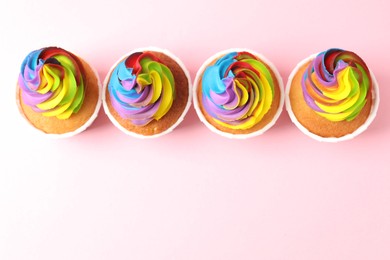 Photo of Delicious cupcakes with colorful cream on pink background, flat lay. Space for text