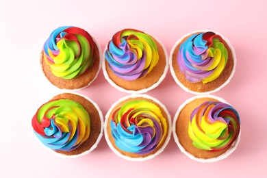 Photo of Delicious cupcakes with colorful cream on pink background, flat lay