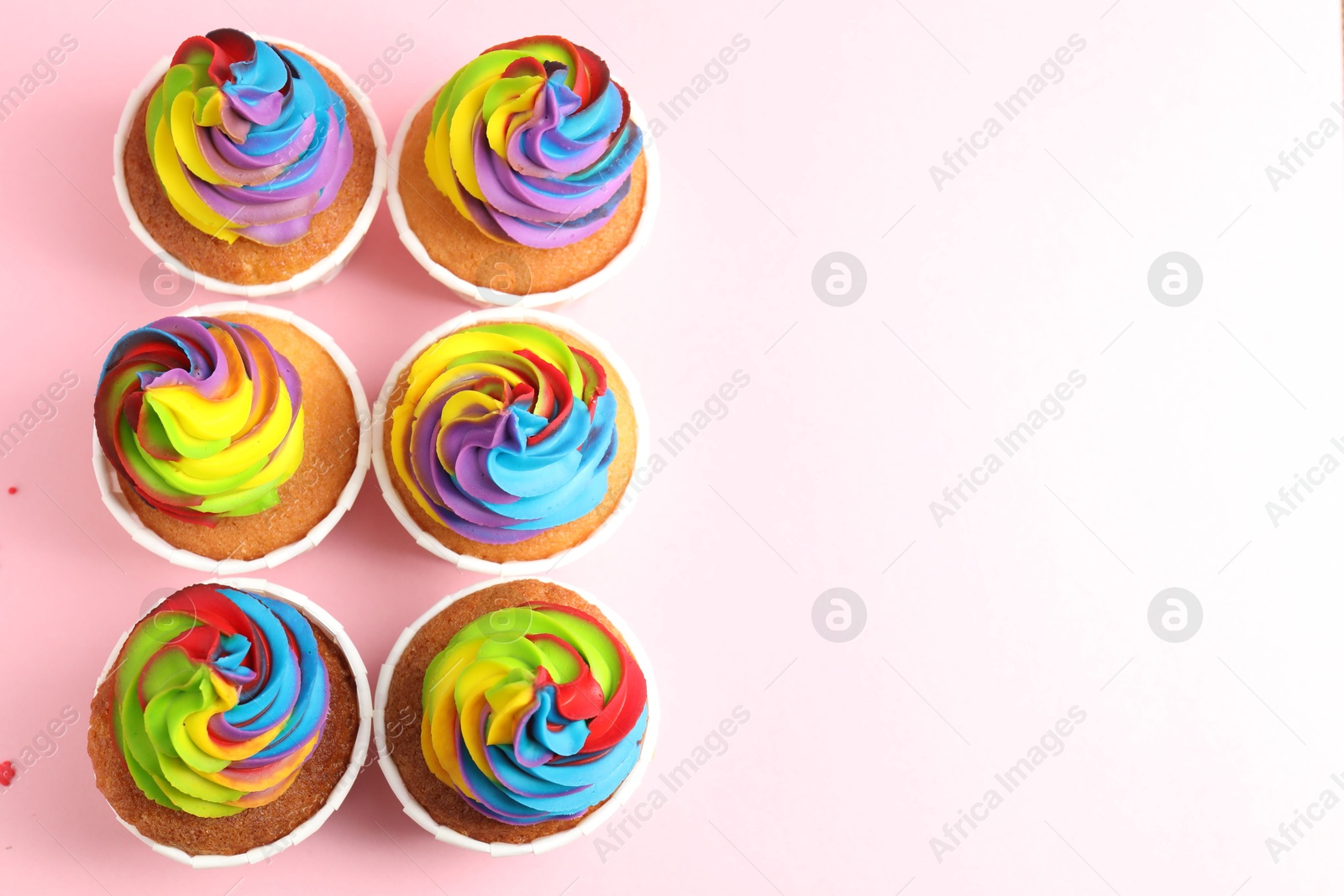 Photo of Delicious cupcakes with colorful cream on pink background, flat lay. Space for text