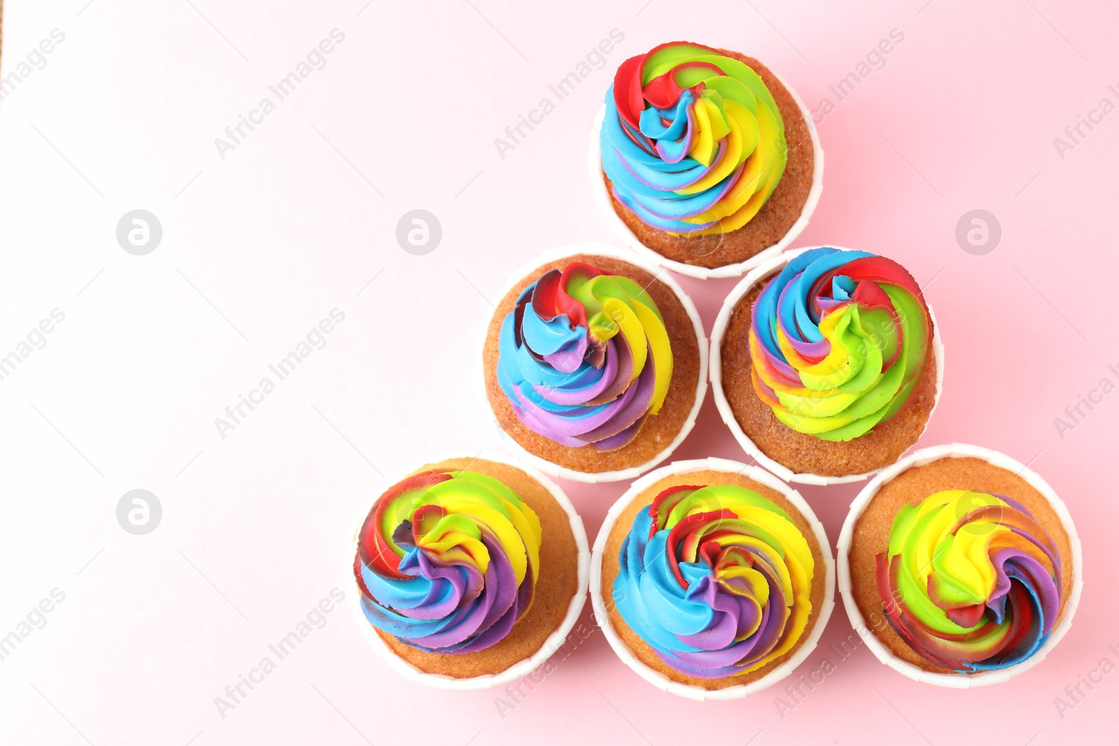 Photo of Delicious cupcakes with colorful cream on pink background, flat lay. Space for text