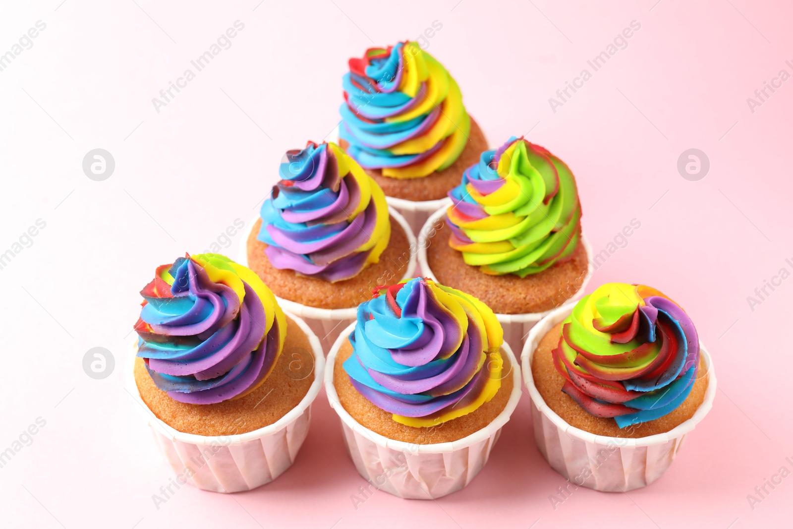 Photo of Delicious cupcakes with colorful cream on pink background, closeup