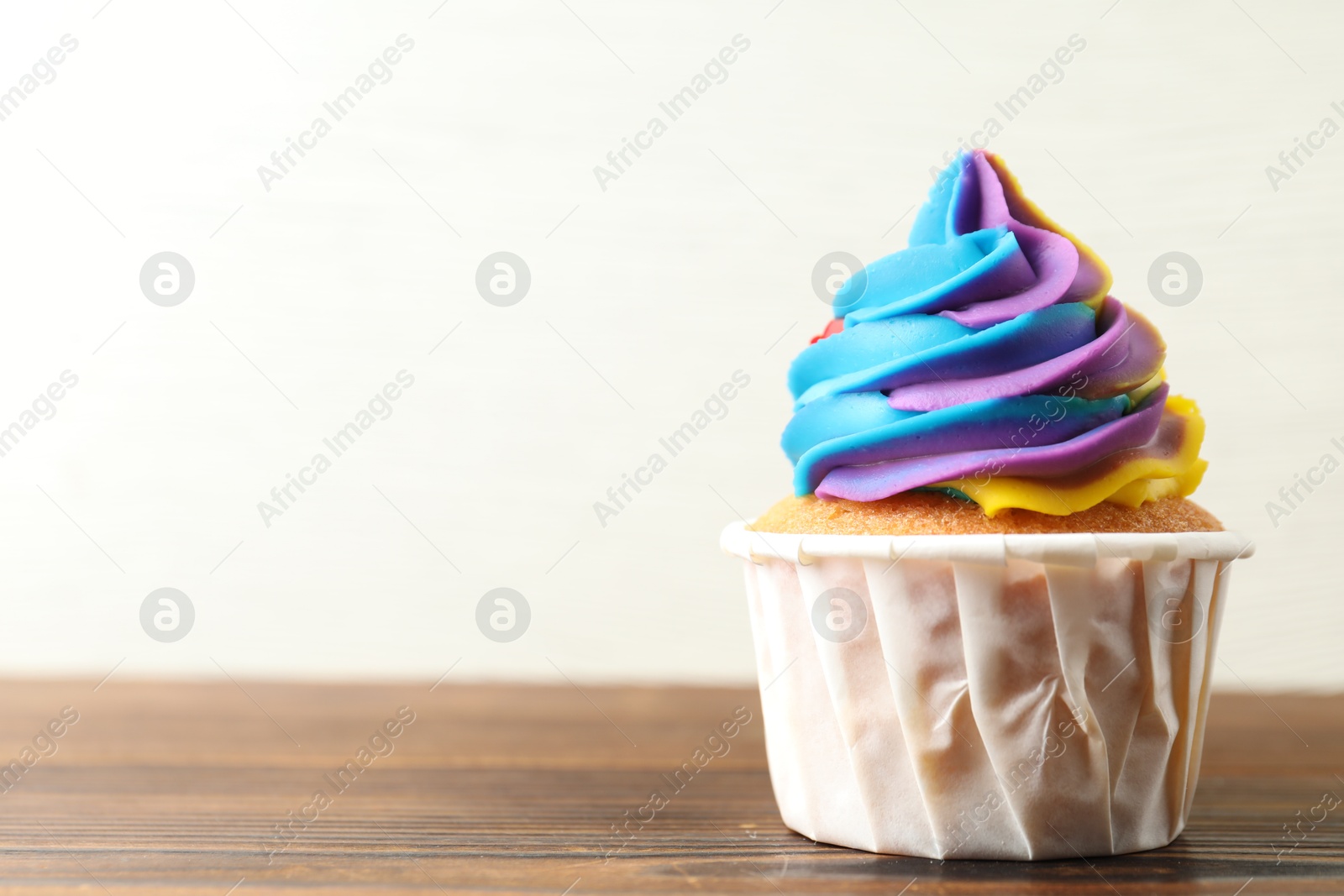 Photo of Delicious cupcake with colorful cream on wooden table against white background, closeup. Space for text