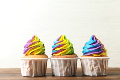 Photo of Delicious cupcakes with colorful cream on wooden table against white background, closeup